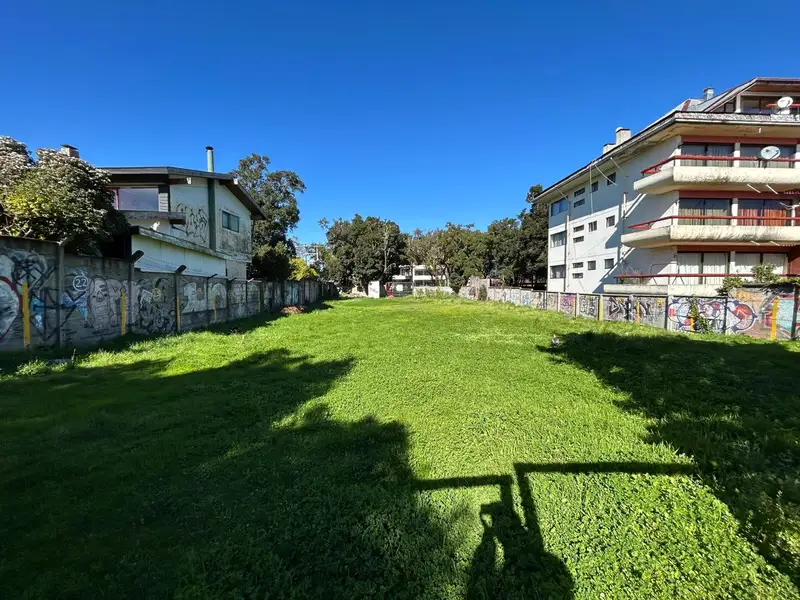 Terreno plano cubierto de pasto en Pucón, entre dos edificaciones y bajo cielo despejado